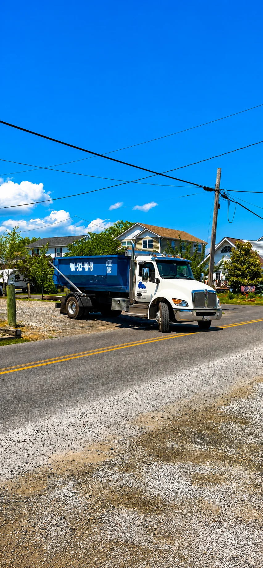 White and blue waste management truck with blue roll-off dumpster on residential street