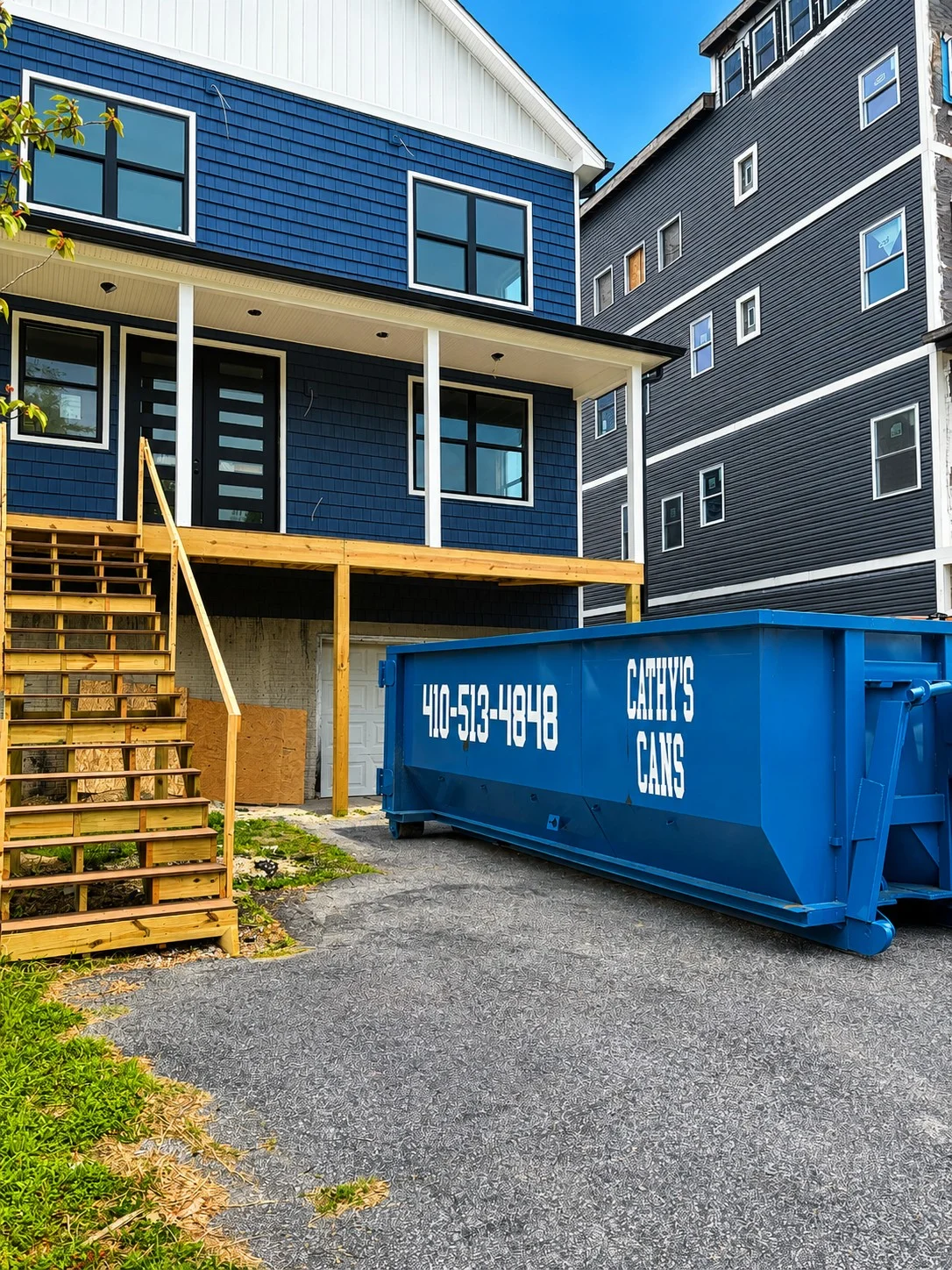 20-yard blue dumpster at residential construction site with wooden deck and new home construction