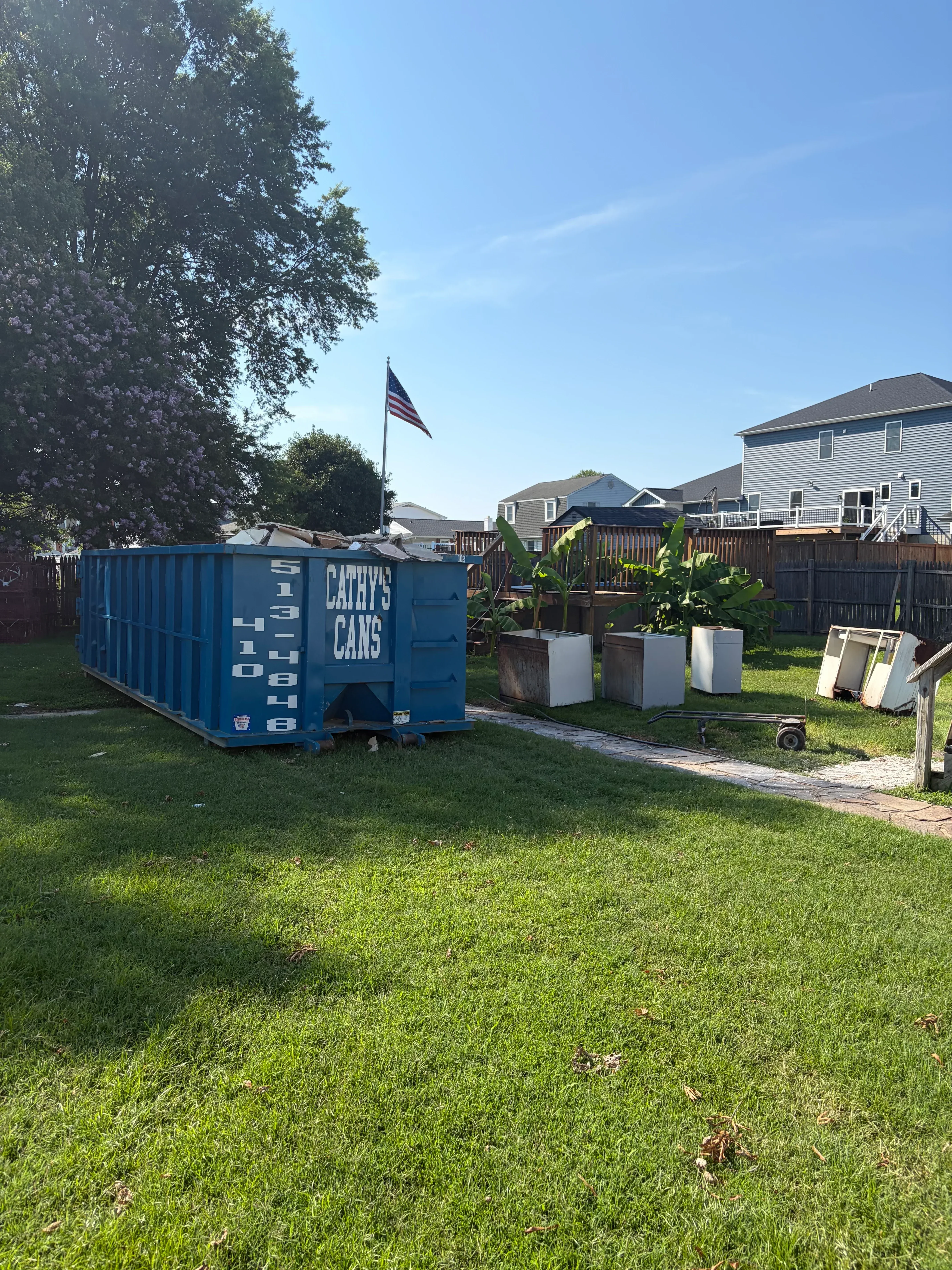 Blue commercial dumpster container on residential property with green lawn and landscaping
