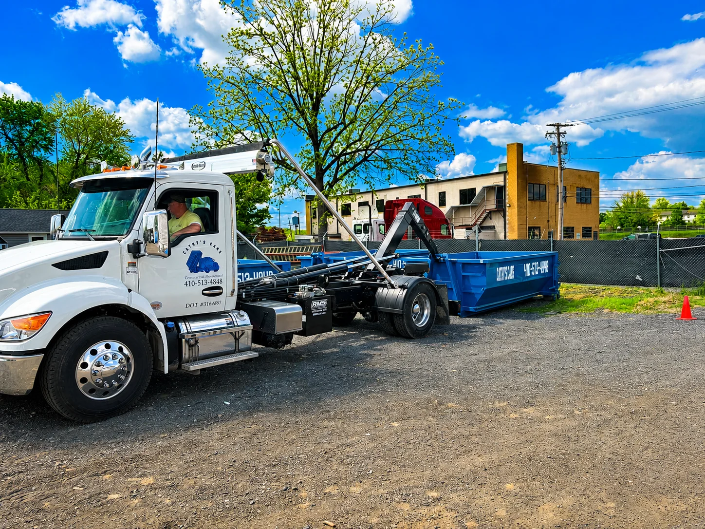 White commercial truck with hydraulic lift arm placing blue roll-off dumpster