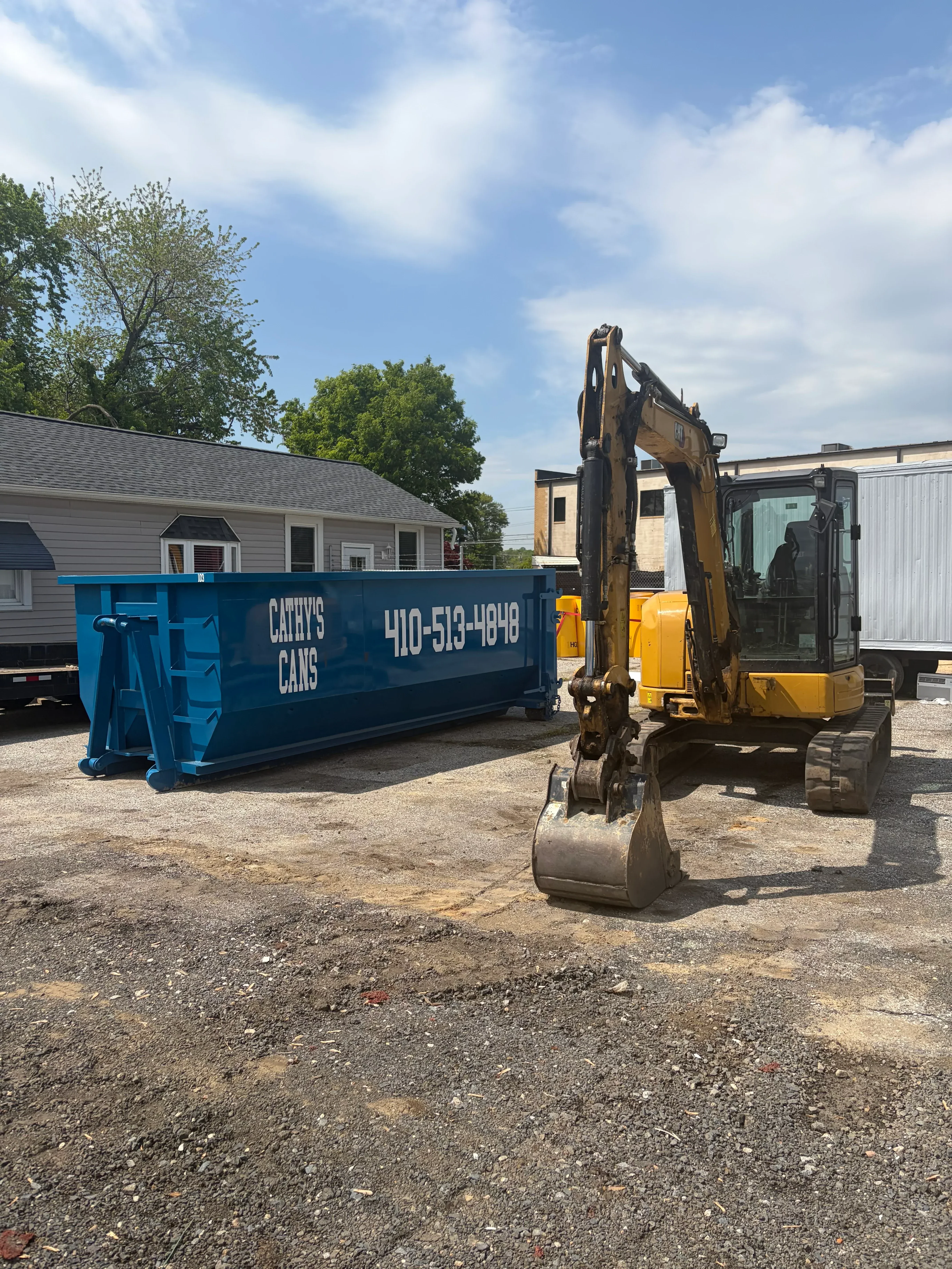Yellow hydraulic dumpster truck with blue waste container at residential property