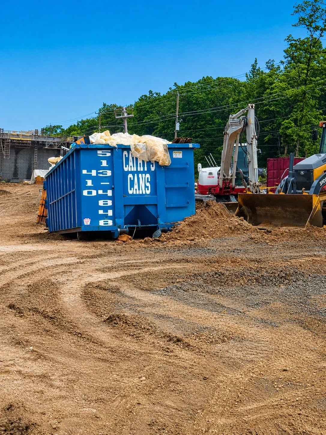 Blue 30-yard dumpster filled with construction waste on prepared gravel site with hydraulic lift truck