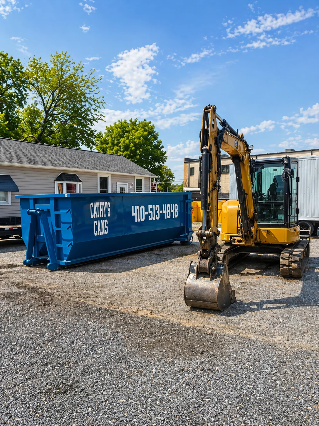 Yellow excavator and blue dumpster container on gravel lot near residential homes