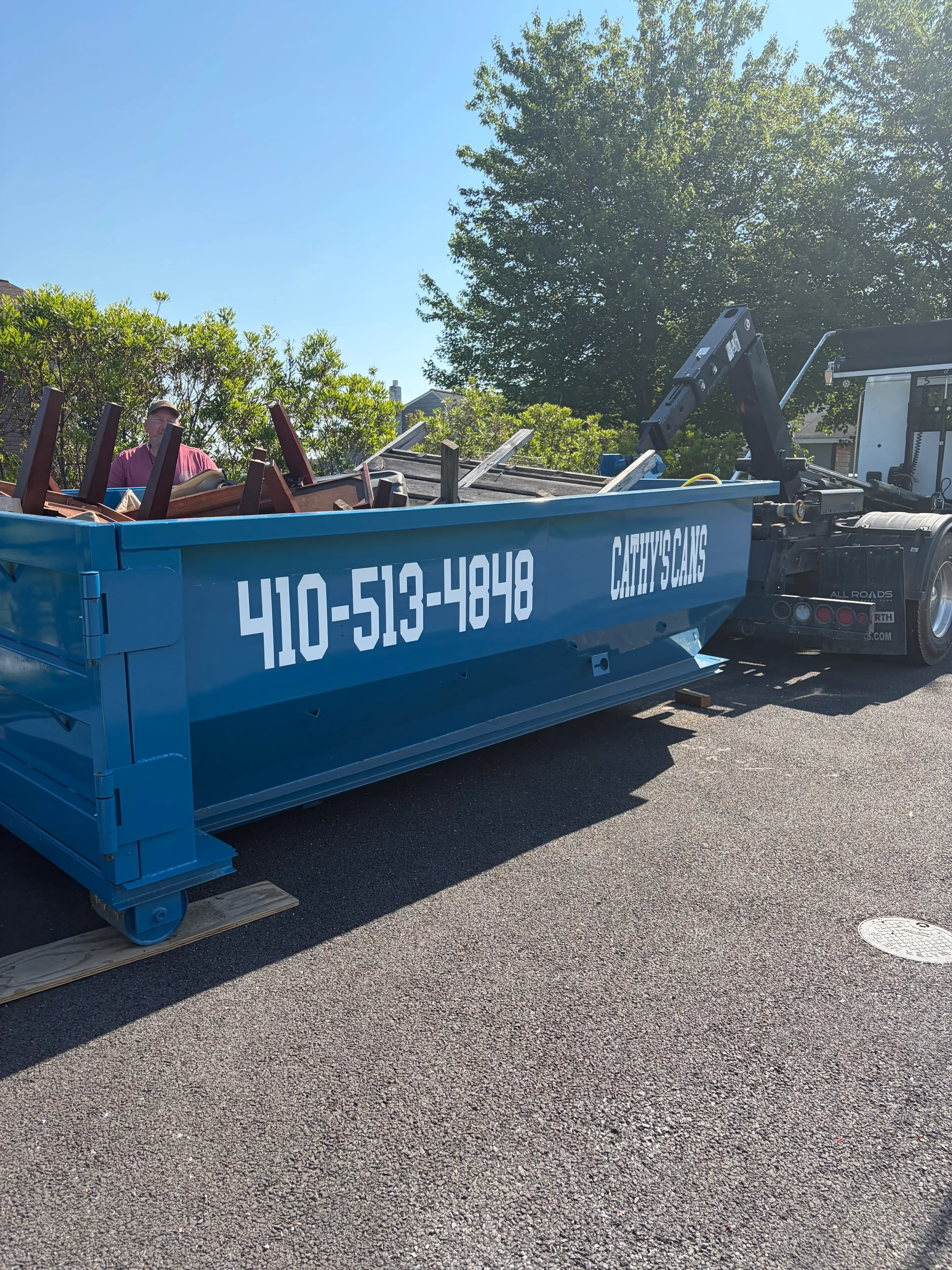 Blue commercial dumpster and waste collection truck with company branding on asphalt