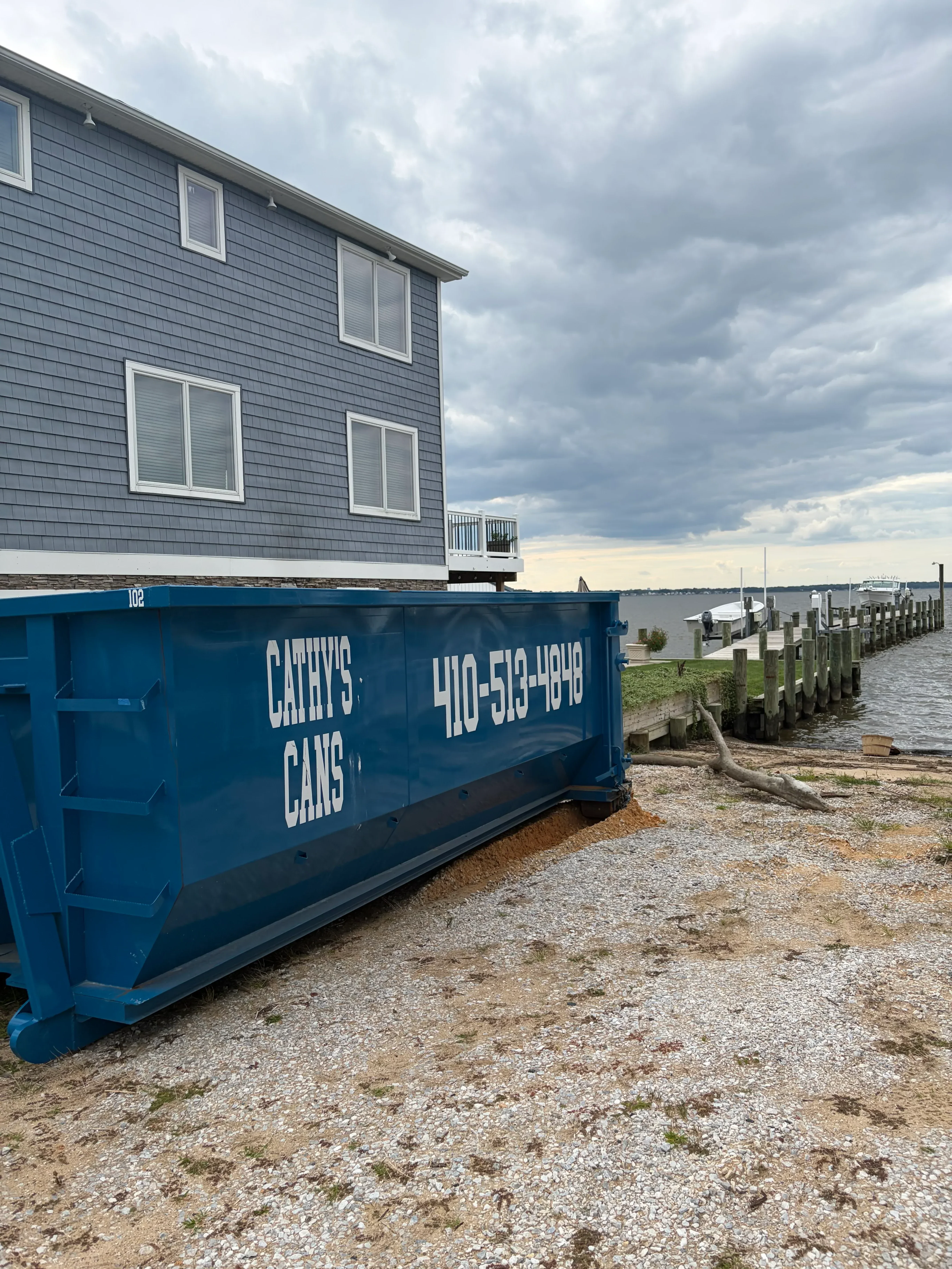 Blue waste container beside residential home with metal roof and white-trimmed windows